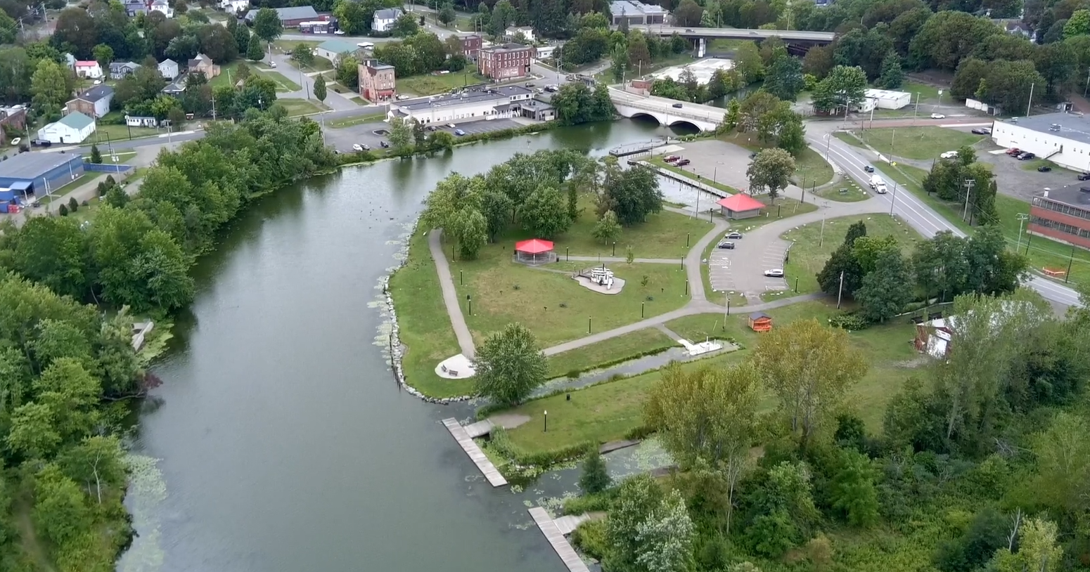 Aerial view of McCrea Point Park with walking paths, docks, picnic shelters, and green space along the Chadakoin River, surrounded by roads and nearby buildings.